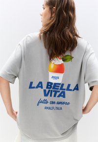 Szürke, túlméretezett póló, amely egy színes gelato grafikával és merész kék felirattal rendelkezik: "LA BELLA VITA", továbbá "fatto con amore" és "AMALFI, ITALIA" feliratokkal.