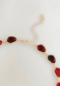 Złota naszyjnik z łańcuszkiem z czerwonymi fasetowanymi klejnotami w kształcie owalnym i łezkowatym, z zapięciem i regulowanym długości łańcuszkiem.