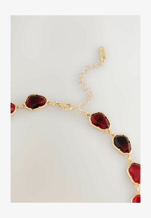 Guldkedja med röda fasetterade ädelstenar i oval och droppform, utrustad med ett lås och en kedja med justerbar längd.