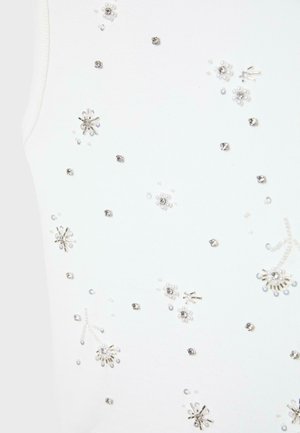 Tessuto bianco con piccoli ornamenti floreali di perline argento e perla disposti a uno schema delicato.