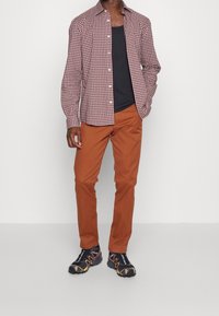 Röd och vit rutigt långärmad skjorta, svart linne, rostfärgade byxor och svarta sneakers med orange detaljer.