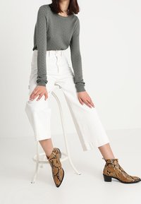 Haut à manches longues texturé gris, pantalons blancs à jambes larges et bottines bordeaux à imprimé serpent avec un bout pointu et un talon bas.