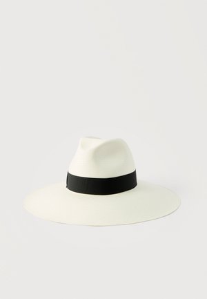 Chapeau blanc à large bord avec une calotte plissée et un ruban noir autour de la base de la calotte, sur un fond clair uni.