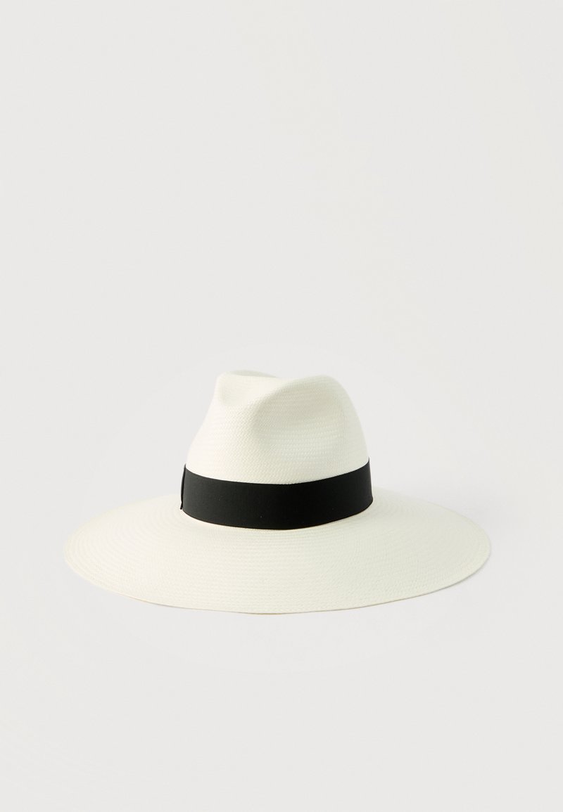 Λευκό καπέλο με ευρύ γείσο, με πτυχωμένη κορυφή και μαύρη κορδέλα γύρω από τη βάση της κορυφής, πάνω σε απλό ανοιχτό φόντο.