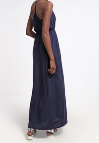 Marineblauwe maxi-jurk met een losse pasvorm, elastische tailleband en dunne schouderbandjes. De stof lijkt glad en lichtgewicht, tot aan de enkels vallend.