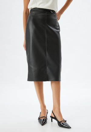 Jupe crayon en cuir noir taille haute, dotée d'une boucle de ceinture circulaire et d'une texture lisse. L'ourlet arrive au genou.