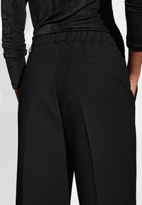 I pantaloni neri presentano un tessuto liscio e testurizzato con una vestibilità comoda e una vita elastica. Inclusa una tasca sul retro e un design a gamba larga.