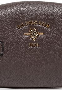 Brun lädernecessär med en texturerad yta, med en guld U.S. Polo Assn. logotyp och metalldetaljer. Rundad topdesign.