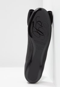 Chaussure plate en cuir noir avec un dessus texturé et une semelle noire lisse et brillante. La semelle présente un marquage en relief et des détails complexes.