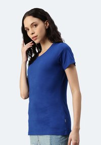 T-shirt blu a maniche corte realizzato in tessuto morbido, con scollatura rotonda, design aderente e un piccolo etichetta decorativa sul fondo laterale.
