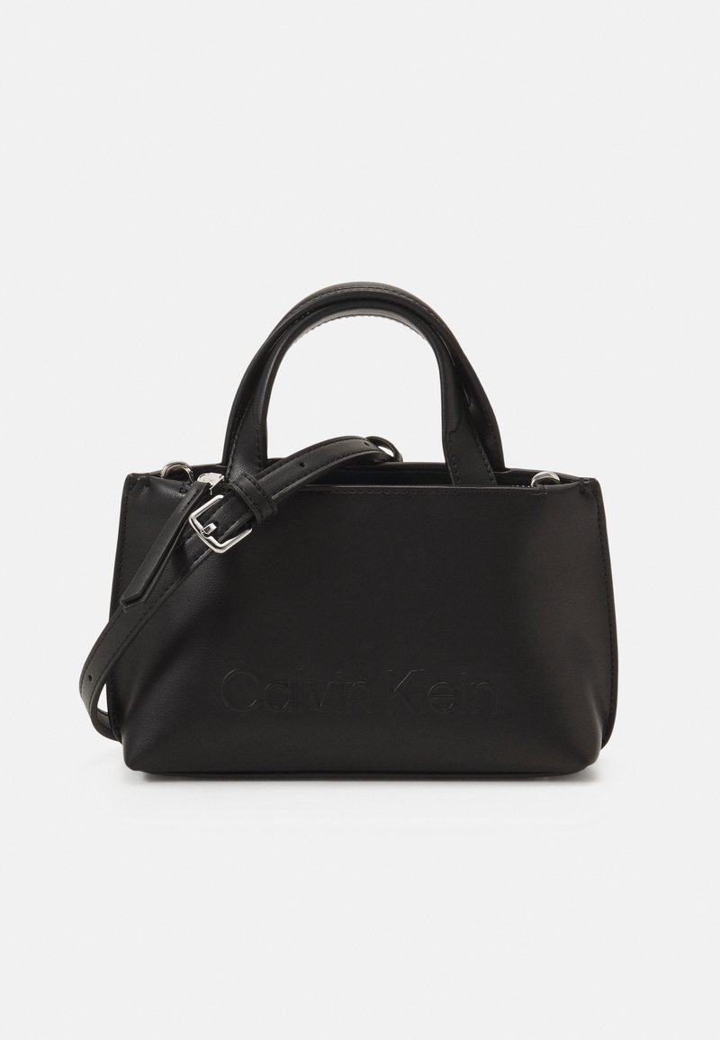 Sac à main rectangulaire noir avec poignées supérieures, bandoulière réglable et nom de marque subtilement embossé à l'avant.