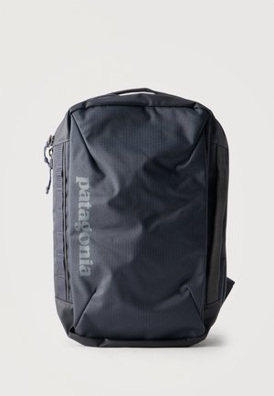 Mochila Patagonia negra con compartimento principal con cremallera, lazos laterales y asa acolchada sobre un fondo claro.