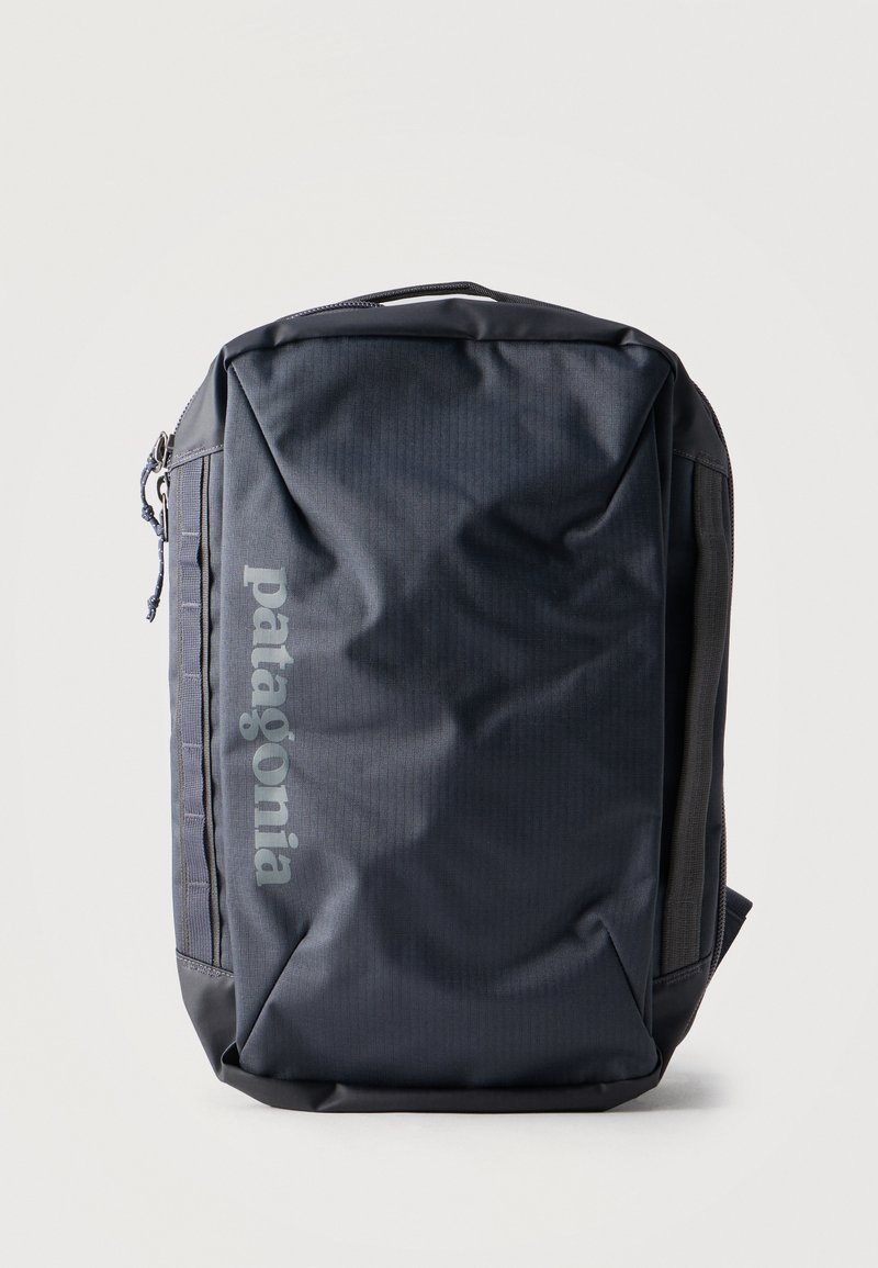 Μαύρο σακίδιο πλάτης Patagonia με φερμουάρ στο κύριο διαμέρισμα, πλαϊνές θηλιές και επενδεδυμένη λαβή σε ανοιχτό φόντο.