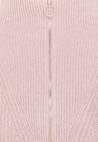 Jasnoróżowy sweter z dzianiny z pionowym prążkowaniem, złotym zamkiem błyskawicznym na środku oraz okrągłym uchwytem do zamka.