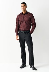 Camicia elegante bordeaux a maniche lunghe con colletto button-down abbinata a pantaloni eleganti neri e scarpe nere; la camicia ha una trama liscia.