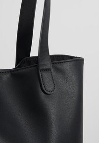 Sac fourre-tout noir en matériau synthétique lisse et texturé. Il est doté de longues poignées plates et d'un design simple et sobre.