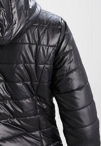 Zwarte gewatteerde jas met een glanzende, gladde textuur. Heeft een capuchon, gewatteerd ontwerp en zichtbare stiknaden op de mouwen.