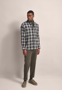 Grün-blau kariertes Hemd mit Button-Down-Kragen, getragen über einem dunkelgrünen Rollkragenpullover. Kombiniert mit olivfarbenen Hosen und beigen Schuhen.