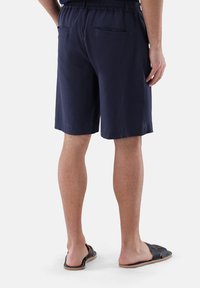 Navyblaue Shorts aus strukturiertem Stoff mit einem elastischen Bund, ausgestattet mit zwei Gesäßtaschen, kombiniert mit schwarzen Badeschlappen.