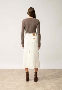 Rybkowany brązowy top z długim rękawem w połączeniu z białą spódnicą midi z denimu z centralnym rozcięciem, uzupełniony brązowymi botkami na grubej szpilce.