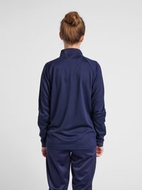 Marineblauwe sporttop van gestructureerde stof, met een hoge kraag en lange mouwen. Gecombineerd met bijpassende marineblauwe broek.
