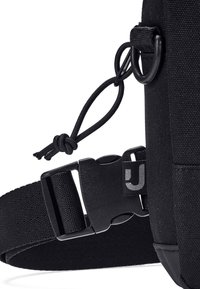 Correa de tela negra para bolsa con hebilla de plástico, cinta ajustable, anilla para llaves y cordón anudado unido a un anillo en D metálico.