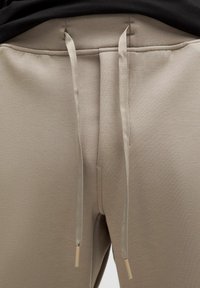 Beige sweatpants med en glat tekstur, elastisk talje med to lyse snore og et minimalistisk design.