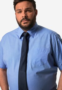 Camisa de manga corta azul claro con un bolsillo y una corbata azul marino, hecha de una tela suave con una sutil textura y un cuello estructurado.