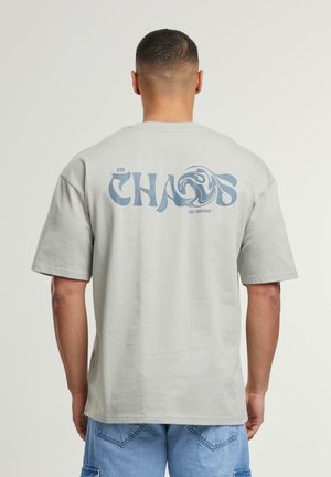 Lichtgrijs katoenen T-shirt met een grote blauwe tekstgrafiek "CHAOS" en een zwirls ontwerp op de achterkant. Korte mouwen en comfortabele pasvorm.