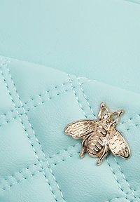 Borsa in finta pelle verde menta trapuntata con accento dorato a forma di ape. Presenta un motivo cucito e una texture liscia, che mette in risalto il design unico.