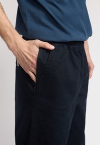Pantaloni neri dal taglio rilassato, con vita elasticizzata e tasche laterali. Realizzati in tessuto morbido, presentano un design pulito senza decorazioni visibili.