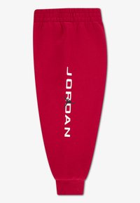 Red jogger pants made of cotton with a tapered fit. Features white "JORDAN" text and a black jumpman logo on the side. Elastic waistband.