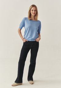 Pulover scurt cu mâneci scurte, de culoare albastru deschis, cu guler rotund, asociat cu blugi evazați din denim închis. Textura moale și croiala lejeră sporește confortul.