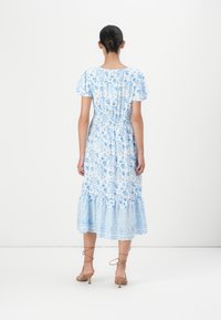 Robe midi à motif paisley bleu et blanc, avec des manches courtes à volants, une taille élastique et un ourlet à volants en tiers. Texture de tissu lisse.