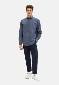 Blaue gemusterte Hemd mit Knöpfen, kombiniert mit maritimen Hosen und weißen Turnschuhen. Das Hemd hat ein dezentes geometrisches Design und einen klassischen Kragen.