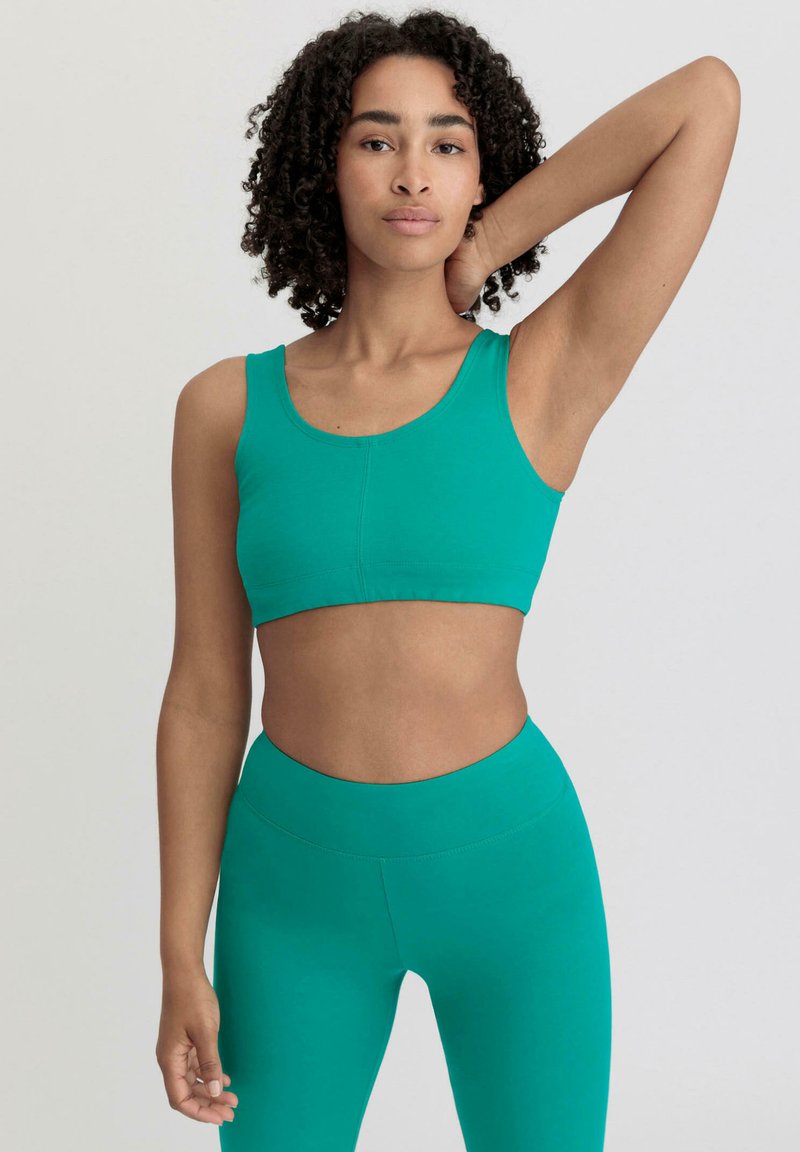 Türkise Sport-BH mit Rundhalsausschnitt und breiten Trägern. Passende hoch-taillierte Leggings, beide aus einem glatten, dehnbaren Material. Keine sichtbaren Muster.
