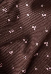 Tejido marrón acanalado con patrones de flores rosas dispersas y tallos verdes, que presenta una apariencia texturada y un diseño floral.