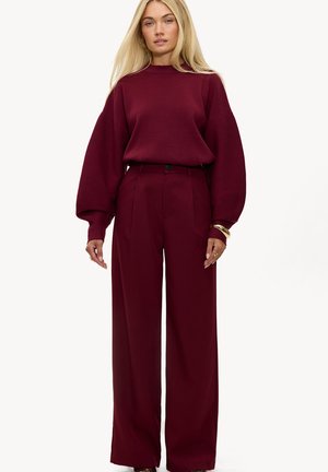 Pull oversize bordeaux avec un col montant et des manches larges, associé à un pantalon large taille haute de la même couleur. Texture lisse.