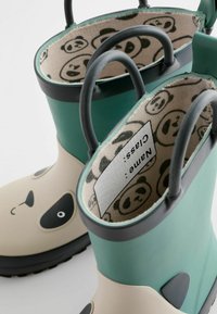 Bottes en caoutchouc vertes avec un design de visage de panda ; l'intérieur présente une doublure à motif avec des illustrations de panda et des poignées noires pour un enfilage facile.