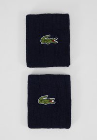 Pulseiras de pulso de tecido felpudo na cor azul-marinho, com um logótipo de crocodilo verde e detalhes em vermelho, empilhadas em duas camadas, com uma superfície texturizada.