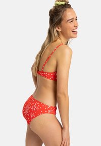 Rdeči bikini set z belimi cvetličnimi vzorci, z nastavljivimi naramnicami in strukturirano površino. Oblika spodnjega dela je zmerna s nabranim dizajnom.