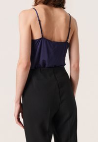 Camisola in satin blu con spalline sottili, texture liscia e vestibilità fluida, abbinata a pantaloni neri a vita alta e su misura.