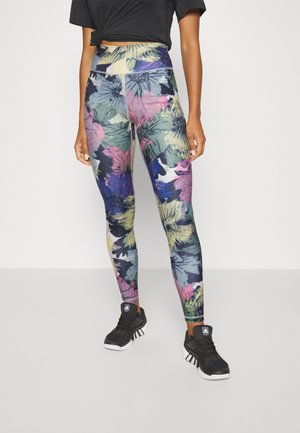 Leggings taille haute avec un motif floral coloré en vert, rose et bleu. Fabriqués en tissu extensible, associés à des chaussures de sport noires.