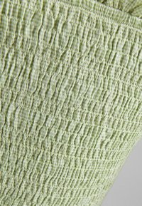 Tessuto verde chiaro testurizzato con un motivo arricciato, che mostra profondità e dimensioni variabili. Superficie liscia con una leggera lucentezza.