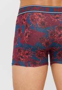 Boxershorts mit einem navyblauen und roten Blumenmuster, einem kontrastierenden elastischen Bund mit Markenlogo, hergestellt aus einem weichen, dehnbaren Material.