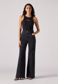 Zwarte tanktop met Levi's-logo, gecombineerd met hooggefdeete, wijde zwarte jeans met een zichtbare knoopsluiting en zijzakken.