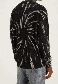 Sudadera negra con estampado de tie-dye que presenta un patrón radial en blanco, de manga larga, cuello redondo y puños y dobladillo acanalados. Textura de tela suave.