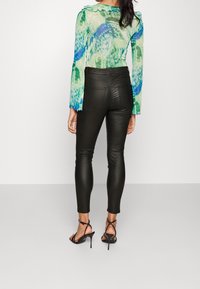 Przezroczysta zielona bluzka z niebieskimi wzorami i falbaniastymi mankietami, w połączeniu z dopasowanymi czarnymi spodniami i czarnymi sandałami na wysokim obcasie ze strapami.