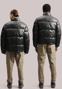 Melns pūkains jakas ar augstu apkakli un paneļu dizainu, apvienots ar bežām kravas biksēm. Jaka ir spīdīga un tai ir elastīgas aproces.