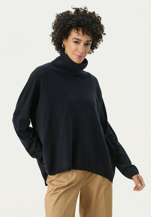 Schwarzer Rollkragenpullover mit lockerer Passform, langen Ärmeln und Rippdetails an den Bündchen und am Saum, kombiniert mit hellbraunen Hosen.